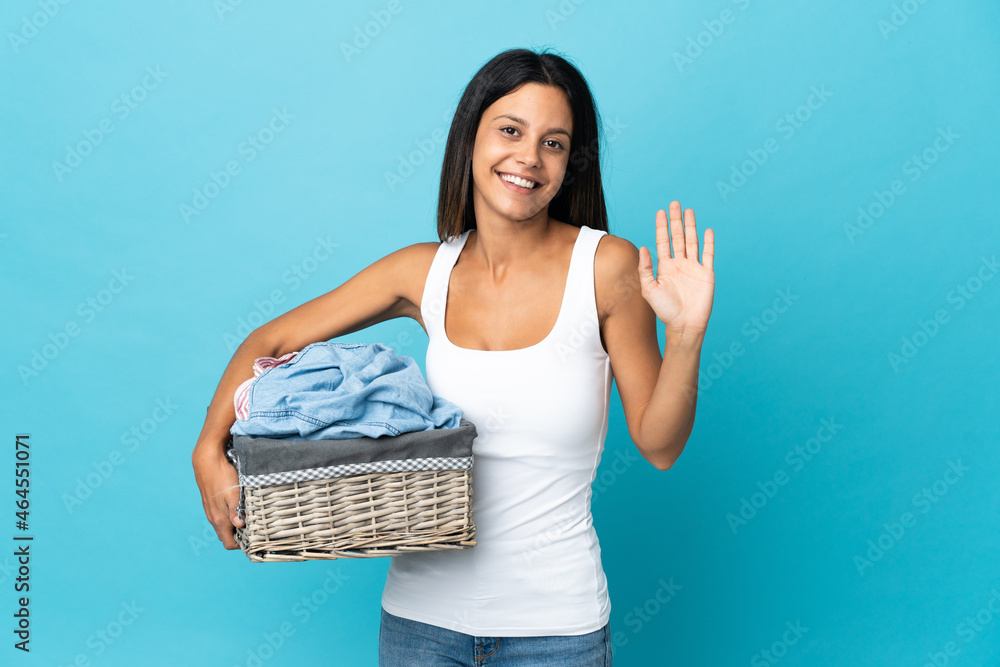 Young woman holding a clothes basket over isolated background saluting with hand with happy expression Young woman holding a clothes basket over isolated background saluting with hand with happy expression