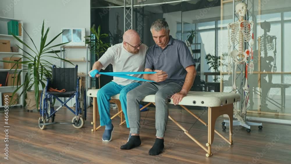 A Physical Therapist Safely Trains the Patient in the Use of Medical Simulators at the Rehabilitation Center. Stiffness in Movement. Elderly Health Support Concept. Medical Services. A Physical Therapist Safely Trains the Patient in the Use of Medical Simulators at the Rehabilitation Center. Stiffness in Movement. Elderly Health Support Concept. Medical Services.