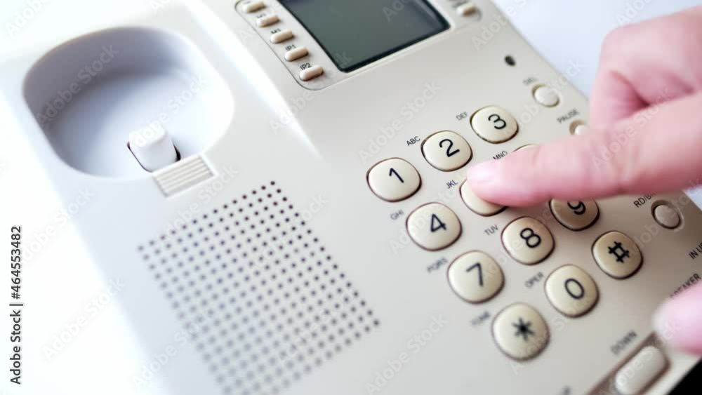closeup female hand presses the buttons of the stationary white office Wired phone, dials the subscriber's number for communication, the concept of hotline help, call center, selective focus closeup female hand presses the buttons of the stationary white office Wired phone, dials the subscriber's number for communication, the concept of hotline help, call center, selective focus