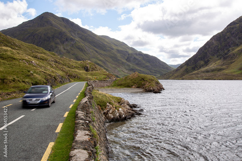 Blurred blue car on the road R335, on the lakeside of Doo Lough, with Ben Gorm in the background, County Mayo, Ireland photo
