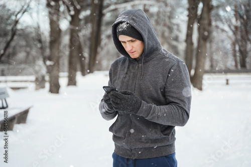 Man athlete using smartphone during winter workout in snowy city park
