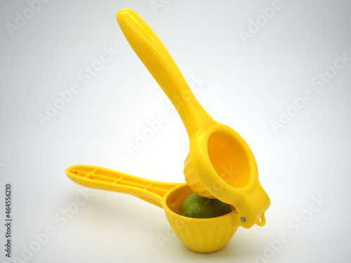 Manual citrus press. Yellow squeezer with green lemon isolated on white background photo