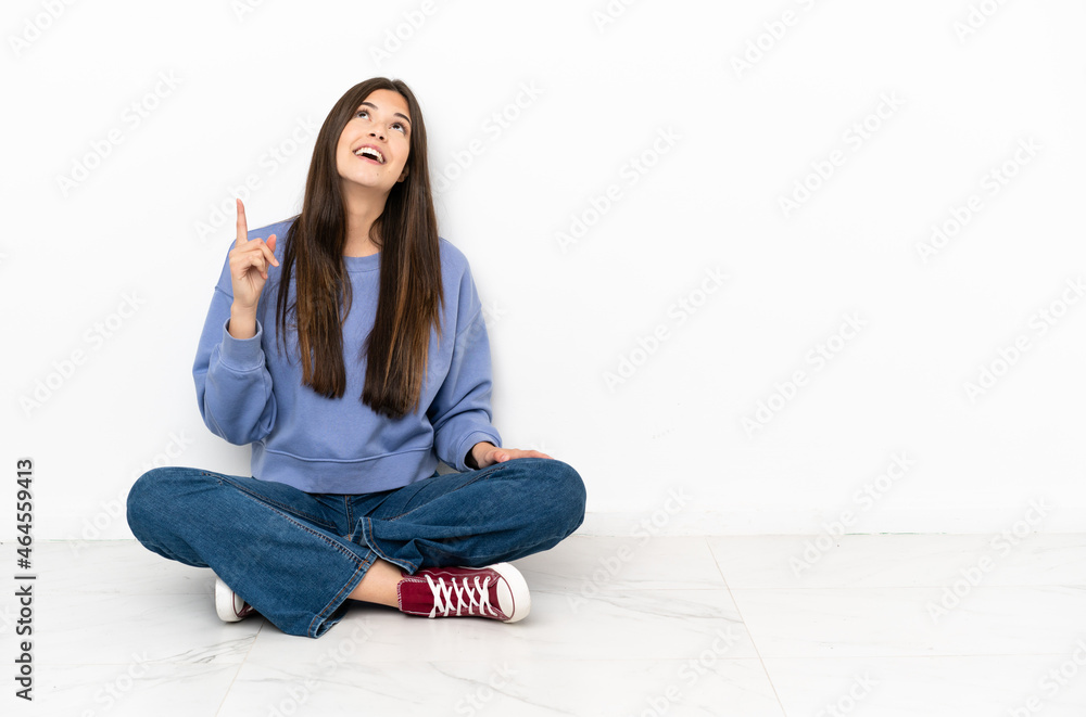 Young woman sitting on the floor pointing up and surprised Young woman sitting on the floor pointing up and surprised