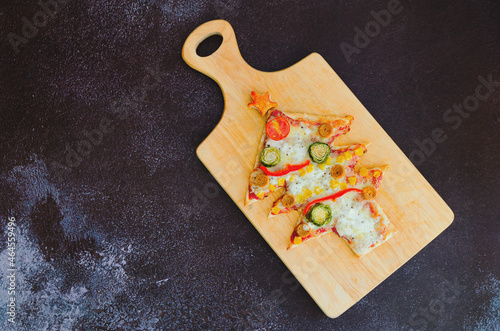 Delicious vegetarian Christmas tree pizza with tomatoes, vegetables and cheese on black background. Creative, funny food concept for kids. Top view, flat lay. Copy space. 