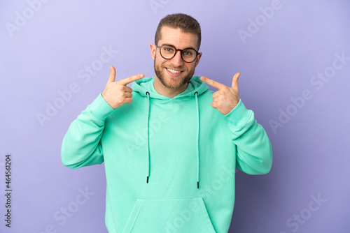 Young handsome caucasian man isolated on purple background giving a thumbs up gesture © luismolinero