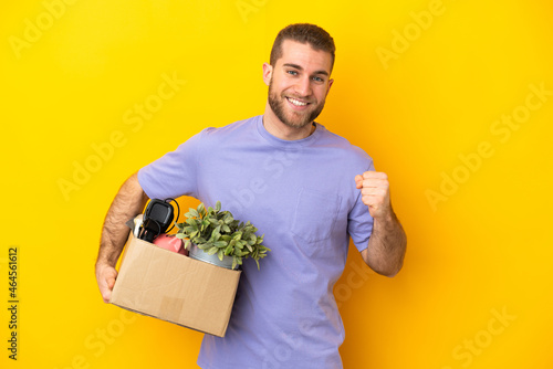 Young caucasian making a move while picking up a box full of things isolated on yellow background celebrating a victory