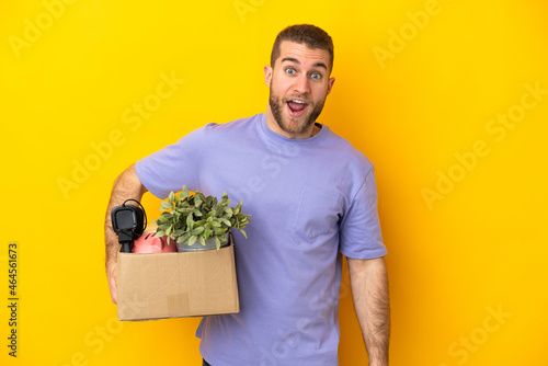Young caucasian making a move while picking up a box full of things isolated on yellow background with surprise facial expression
