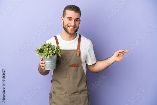 Gardener caucasian man holding a plant isolated on yellow background pointing finger to the side