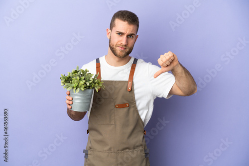 Gardener caucasian man holding a plant isolated on yellow background showing thumb down with negative expression