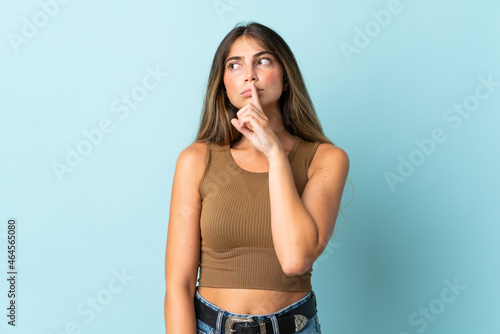 Young caucasian woman isolated on blue background showing a sign of silence gesture putting finger in mouth © luismolinero