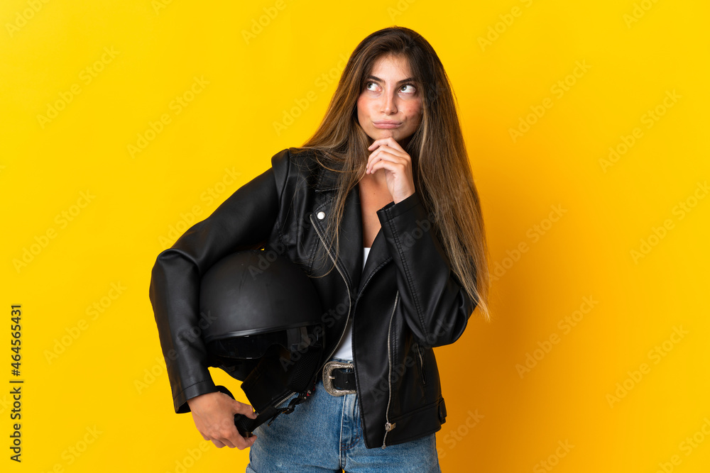 Woman holding a motorcycle helmet isolated on yellow background and looking up Woman holding a motorcycle helmet isolated on yellow background and looking up