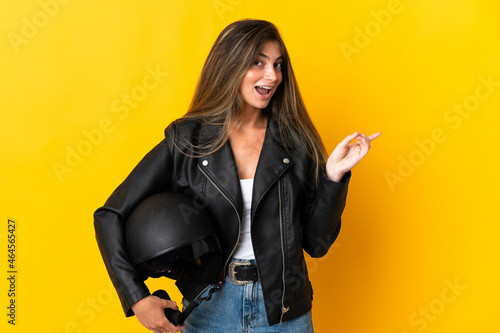 Woman holding a motorcycle helmet isolated on yellow background pointing finger to the side © luismolinero