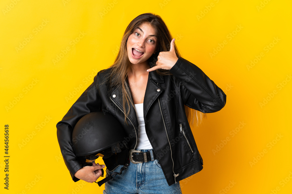Woman holding a motorcycle helmet isolated on yellow background making phone gesture. Call me back sign Woman holding a motorcycle helmet isolated on yellow background making phone gesture. Call me back sign