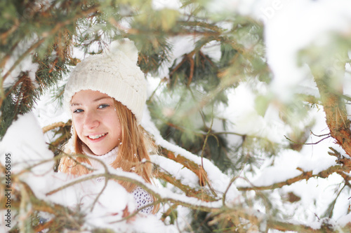 a happy girl in a knitted sweater and a white hat among the snow-covered branches of trees © Марина Мартинез