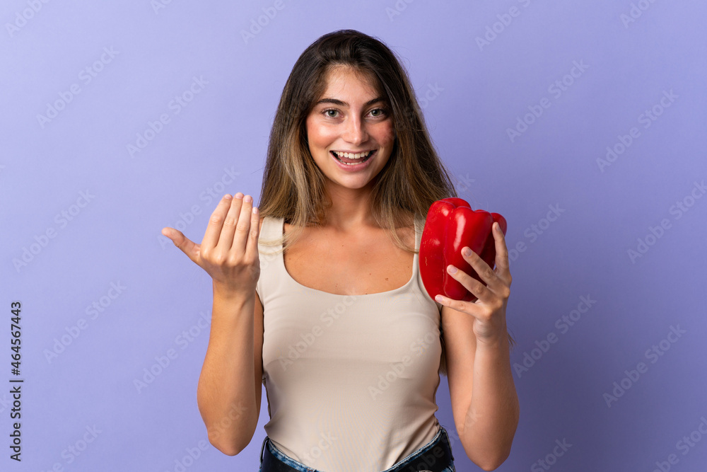 Young woman holding a pepper isolated on purple background inviting to come with hand. Happy that you came Young woman holding a pepper isolated on purple background inviting to come with hand. Happy that you came