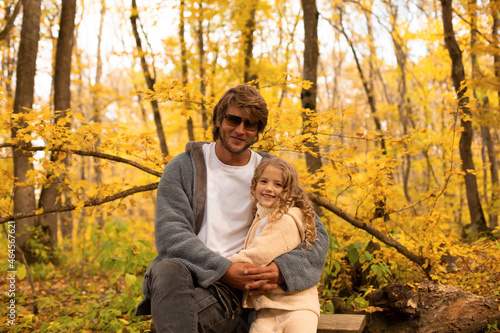 a little blonde girl in a knitted suit hugs her dad with glasses in a gray knitted jacket in the autumn forest © Тамара Киреева