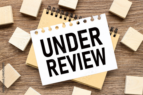 UNDER REVIEW. text on white paper on wood background business concept