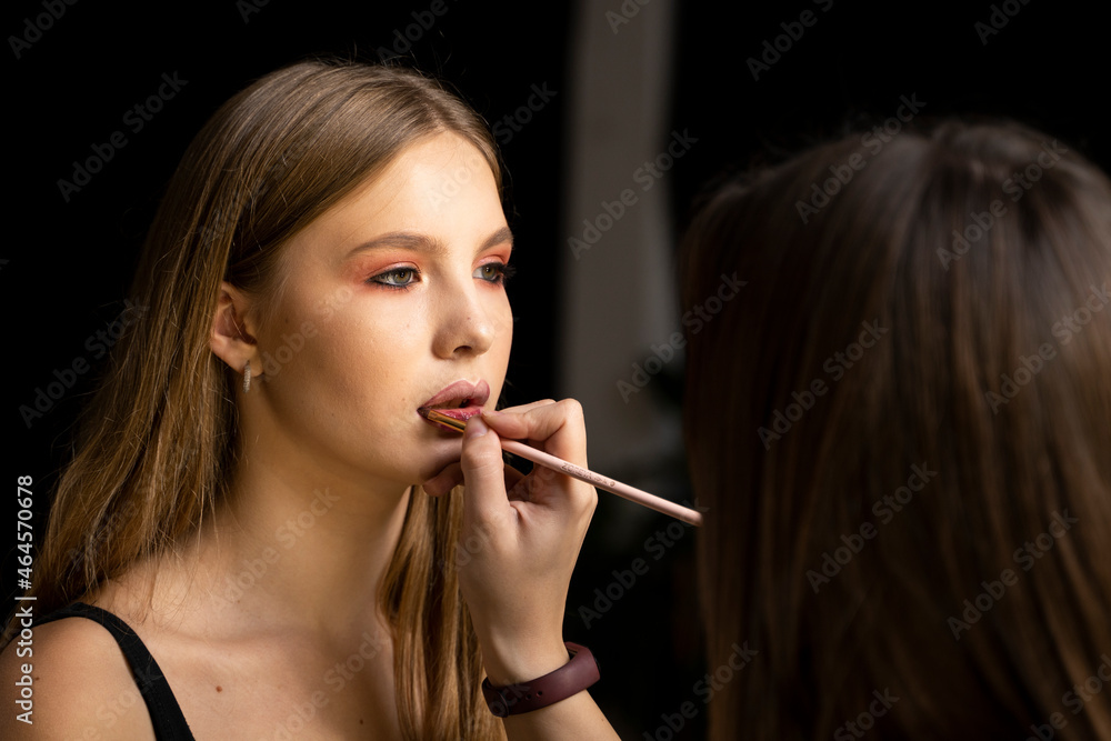 Makeup artist applies red lipstick on a beautiful woman face. Hand of make-up master, painting lips of young beauty model girl. Make up in process. Makeup artist applies red lipstick on a beautiful woman face. Hand of make-up master, painting lips of young beauty model girl. Make up in process.