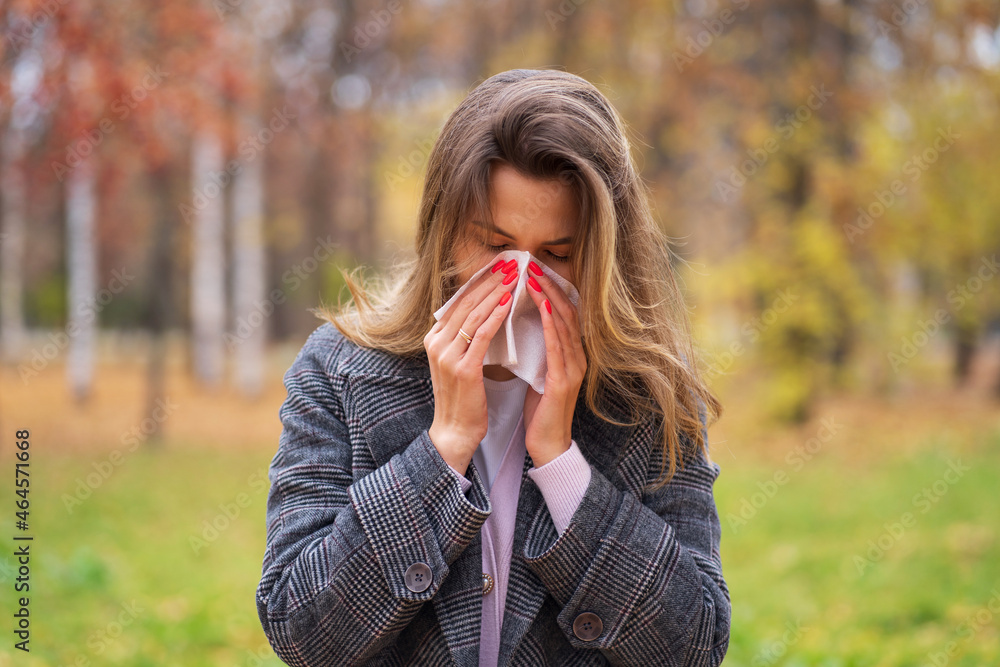 A girl stands on the street in a park in autumn and blows her nose in a handkerchief A girl stands on the street in a park in autumn and blows her nose in a handkerchief