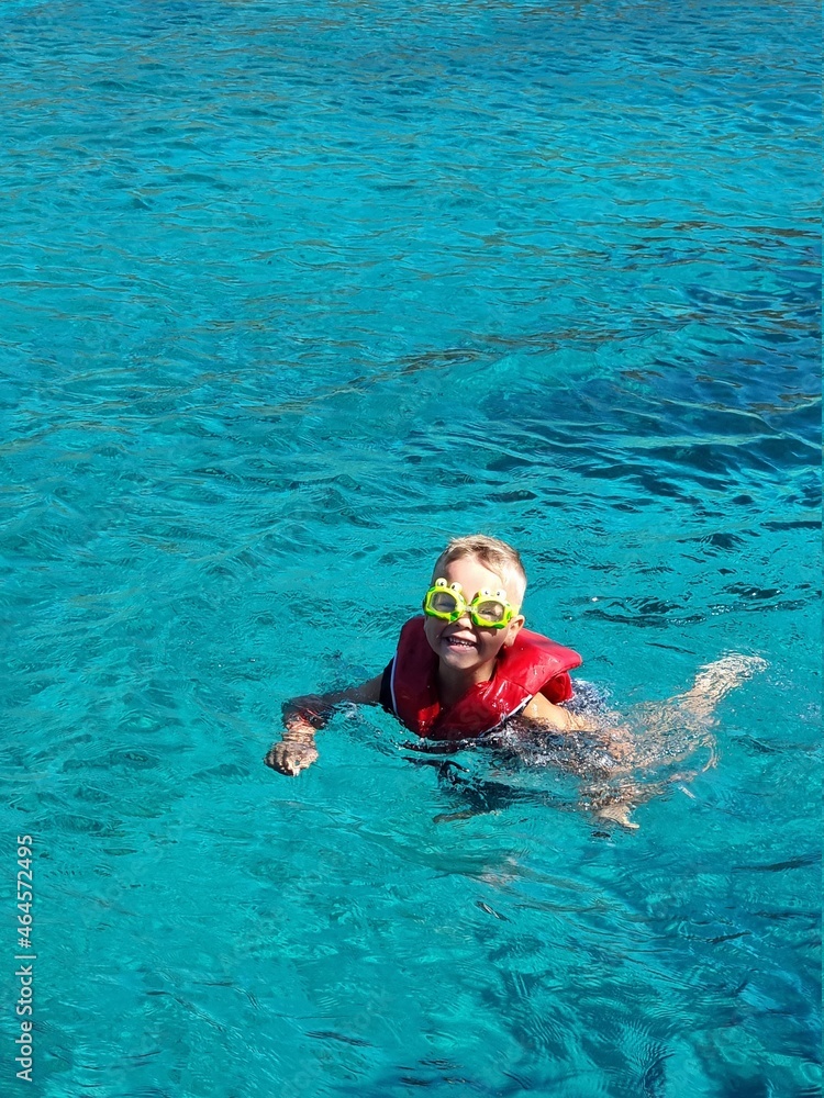 A child in swimming goggles and jelly bathes in the sea. Blue clear water.