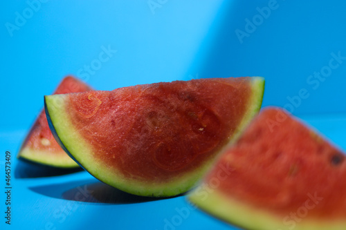 Close-up view of fresh ripe watermelon slices on blue background with highlight and shadow contrast in the morning. Tropical fruits, healthy eating, and summer background concept.