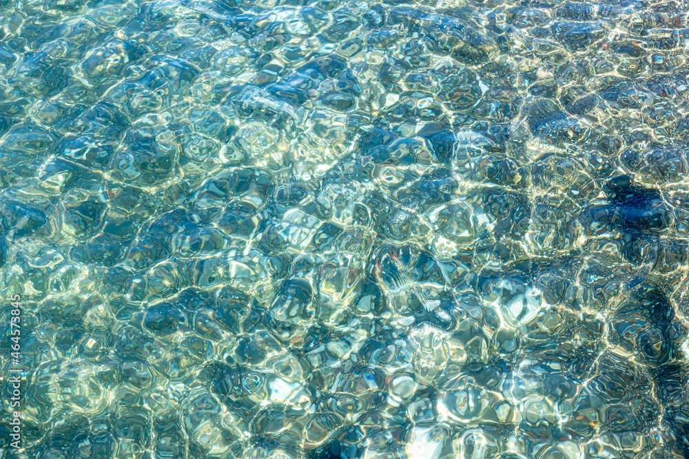 Obraz premium Texture of turquoise sea water in the shoal with visible sandy and pebble bottom. Original background, natural pattern. Close-up with selective focus