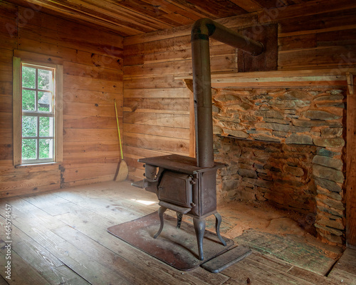 Interior of a primitive log cabin with a wood stove and stone fireplace and wood plank floors and window