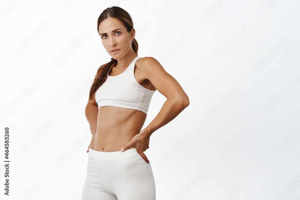 Strong female athlete, middle aged fitness woman in sportsbra, showing her and muscles, exercising in gym, standing over white background Strong female athlete, middle aged fitness woman in sportsbra, showing her and muscles, exercising in gym, standing over white background