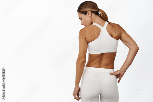 Rear view of middle aged sports woman back, masculine and fit body, standing in activewear against white background