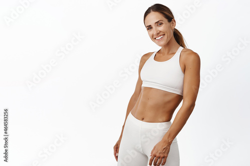 Middle aged woman doing fitness workout, standing in activewear with abs and muscles, smiling happy, standing over white background