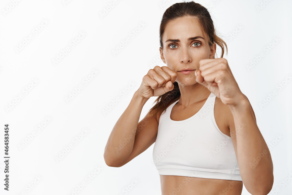 Portrait of fitness woman, female athlete exercising punches, fighting and boxing, standing with clenched fists in defensive pose, white background Portrait of fitness woman, female athlete exercising punches, fighting and boxing, standing with clenched fists in defensive pose, white background