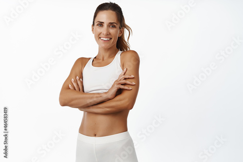 Wallpaper Mural Sport and women health. Smiling sportswoman with abs and muscles in sportsbra, cross arms on chest, looking confident at camera, workout indoors, white background Torontodigital.ca