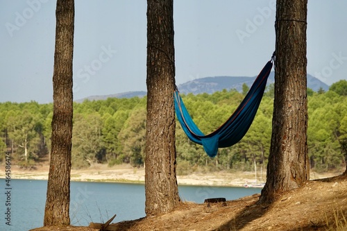 Blue hammock hanging between two trees with the water of a lake in the background