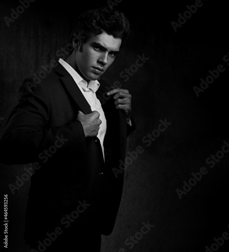 Thinking charismatic man posing and looking serious on dark shadow dramatic light background. Closeup. Art light and shadow.