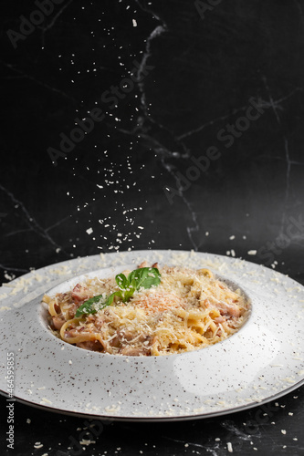Obraz na płótnie Cheese falling on pasta. Spaghetti with bacon, parmesan, cream sauce and egg yolk on black marble background. Mediterranean gourmet food. w salonie