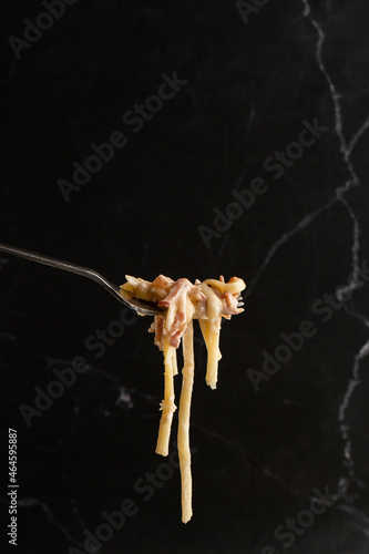 Obraz na płótnie Pasta Carbonara on fork isolated. Spaghetti with bacon, parmesan, cream sauce and egg yolk on black marble background. Mediterranean gourmet food. w salonie