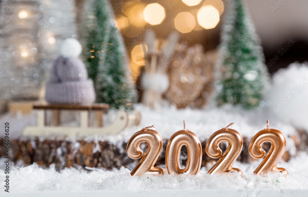 Happy New Year 2022. Beautiful background with candles, a sled with a knitted hat, Christmas trees and decorations. Celebrating the winter Christmas holidays. The concept of the beginning of the year. Happy New Year 2022. Beautiful background with candles, a sled with a knitted hat, Christmas trees and decorations. Celebrating the winter Christmas holidays. The concept of the beginning of the year.