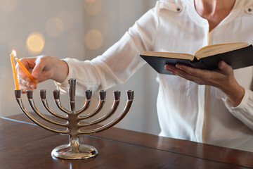Woman lighting first candle of Chanukah on Menorah with the shamash