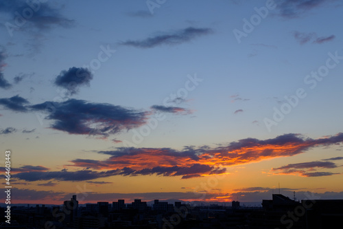 都市の夜明け、早朝ビルの隙間から太陽が昇り辺りはオレンジ色に染まる。ビルはシルエットに浮かぶ