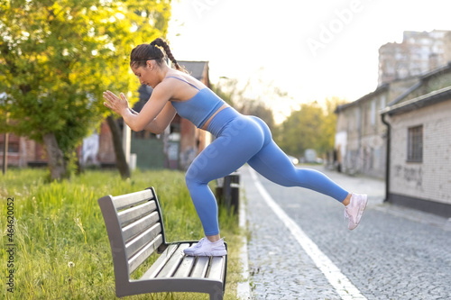 Young fitness female model in blue training sportswear doing leg step ups on bench in street city valley. photo