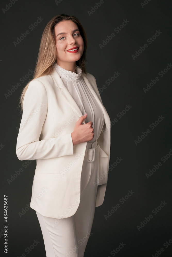 woman suit and skirt white outfit -  studio portrait of attractive beautiful girl dark background. long hair, a hand holds a jacket side, looks straight in a camera smiles. Blurred details