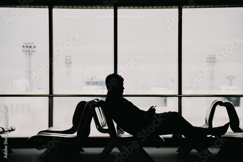 Silhouette of the traveler inside airport terminal. Passenger sitting in a lobby airport waiting for his flight.