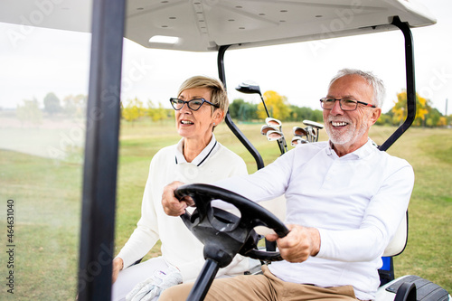 Portrait of healthy retired senior couple driving golf car to the green zone and enjoying free time outdoors. photo