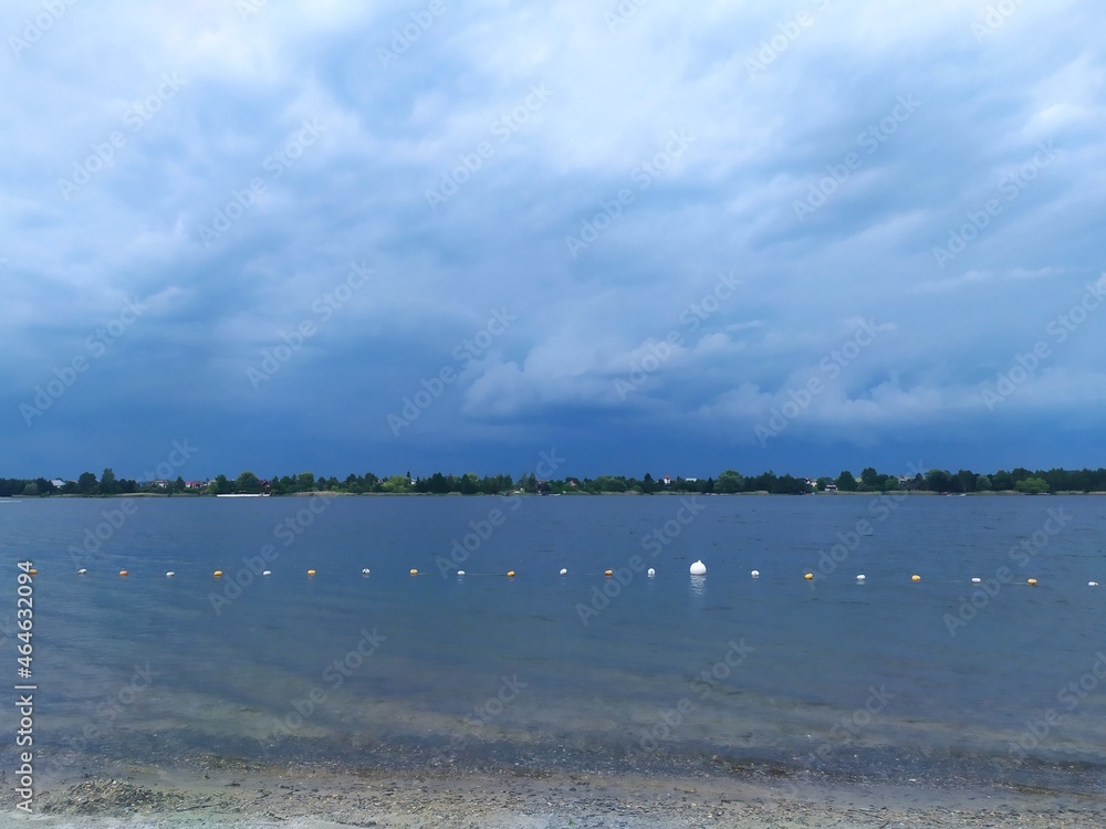 Clouds over the lake, beautiful lake and gloomy sky. Sunny day, the beginning of a thunderstorm.