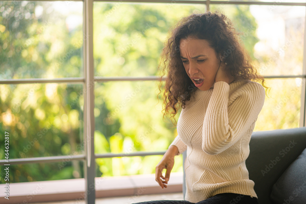 Latin woman sitting on sofa with neckache feeling Latin woman sitting on sofa with neckache feeling