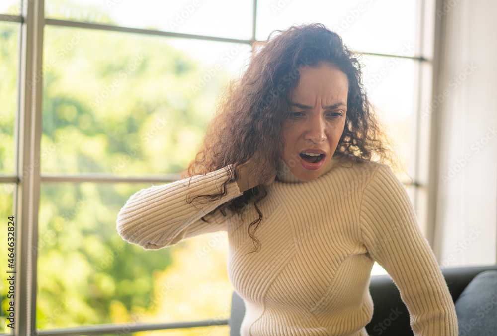 Fototapeta premium Latin woman sitting on sofa with neckache feeling