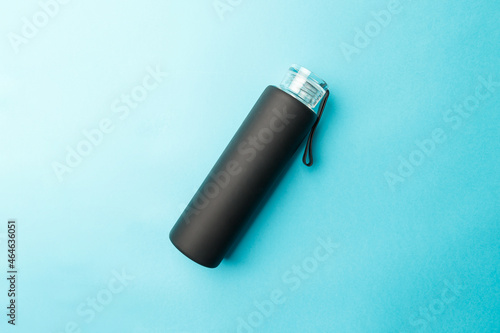 Stylish reusable eco-friendly glass bottle with a black rubberized surface on a blue background. Space for text. Top view. Flat lay. The concept of a lifestyle without plastic and waste