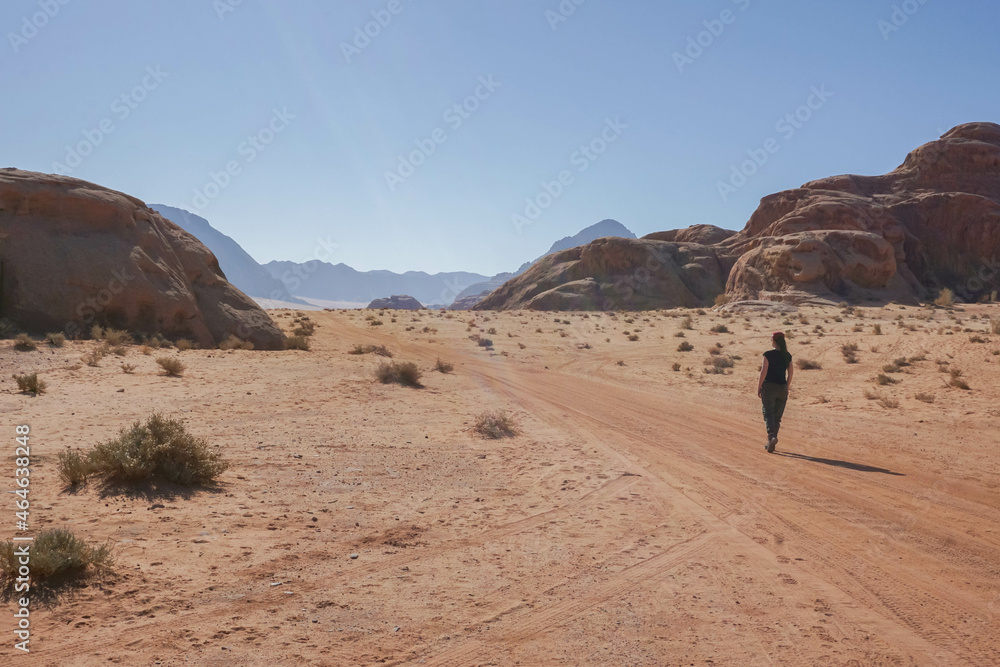A girl walks on an empty road in the Wadi Rum desert, a clear cloudless day, Jordan
