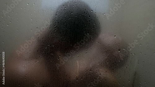 silhouette of lovers in shower, view through wet glass, kiss and embrace of naked people photo