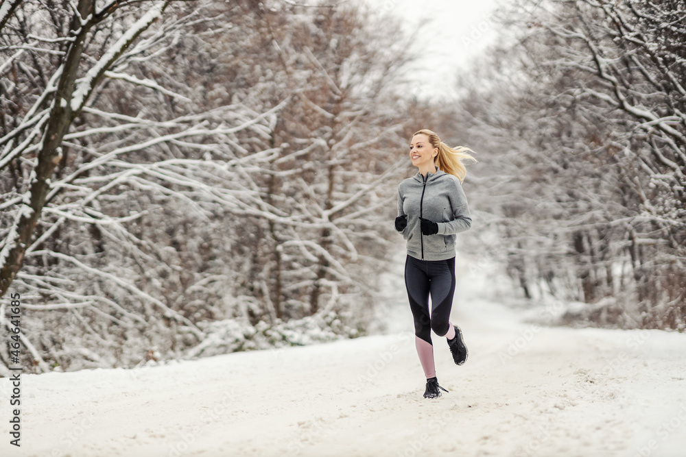Full length of happy middle-aged woman running in nature on snowy path at winter. Winter fitness, healthy habits Full length of happy middle-aged woman running in nature on snowy path at winter. Winter fitness, healthy habits